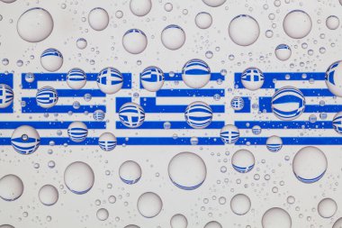 Yağmur damlaları ile kaplı bir cam arkasında Yunan bayrakları.