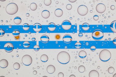 Yağmur damlaları ile kaplı bir cam arkasında Arjantin bayrakları.