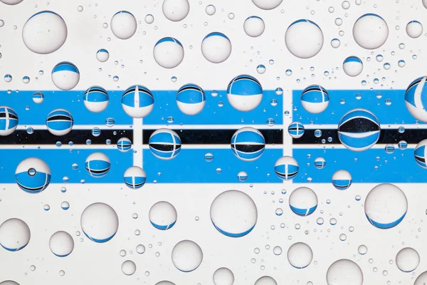 Yağmur damlaları ile kaplı bir cam arkasında Botsvana bayrakları.