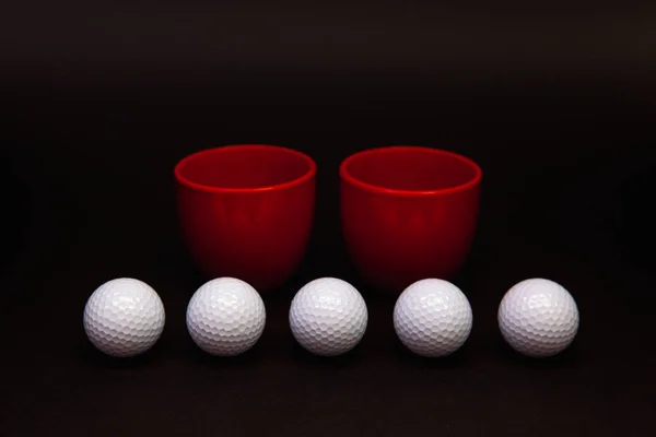 White golf balls and red cups of tea on the black table. — Stockfoto