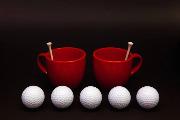 Bílé golfové míčky a červené šálky čaje na černém stole. — Stock fotografie