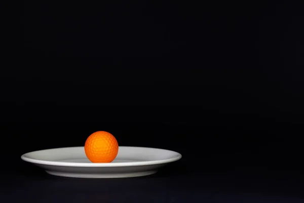 Siyah masa üzerinde beyaz plaka ve turuncu golf topu — Stok fotoğraf