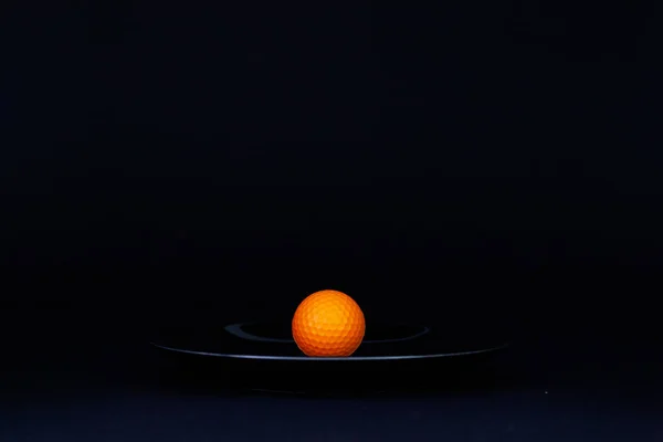 Svart platta och orange golfboll på det svarta bordet — Stockfoto
