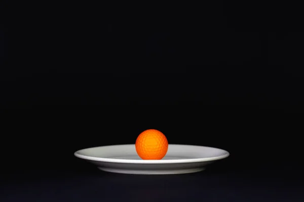 Fehér lemez és narancssárga golflabda a fekete asztalon — Stock Fotó