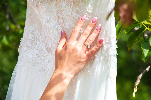 White wedding dress on a background of nature. The bride holds her hand on the wedding dress