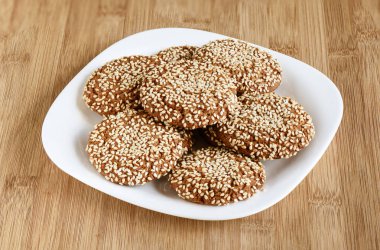 Oatmeal cookies with sesame seeds in a white dish on a wooden ba clipart