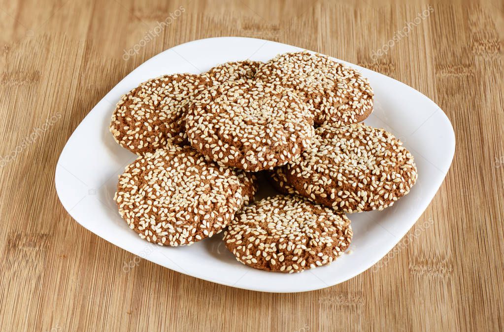 Oatmeal cookies with sesame seeds in a white dish on a wooden ba