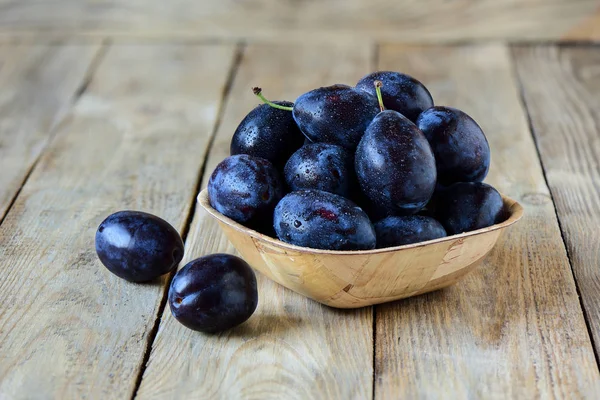 Ripe blue plums in a wooden bowl on a wooden background. Summer seasonal fruit concept. Rustic style.