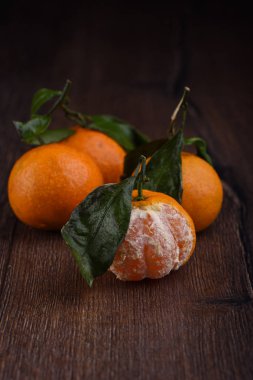 Üç taze mandalina yaprakları ve bir yarı ahşap bir masaya soyulmuş. Rustik tarzı