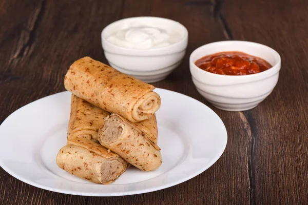 Pancake rolls with meat filling, served with sour cream and ketchup sauce. Traditional russian food on wooden background