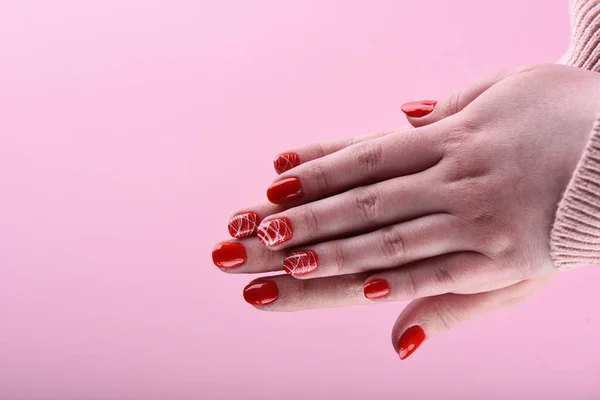 Hands of a girl with a red manicure on her nails. Palm girl on a pink background.