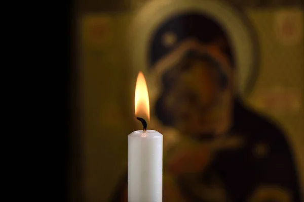 Burning candle in front of the icon of the Mother of God and baby Jesus in the background. Focus on the flame. — Stock Photo, Image