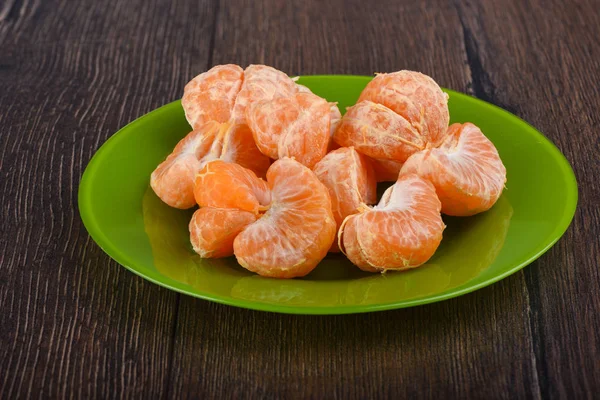 Rebanadas peladas de mandarina en un plato verde sobre una mesa de madera — Foto de Stock