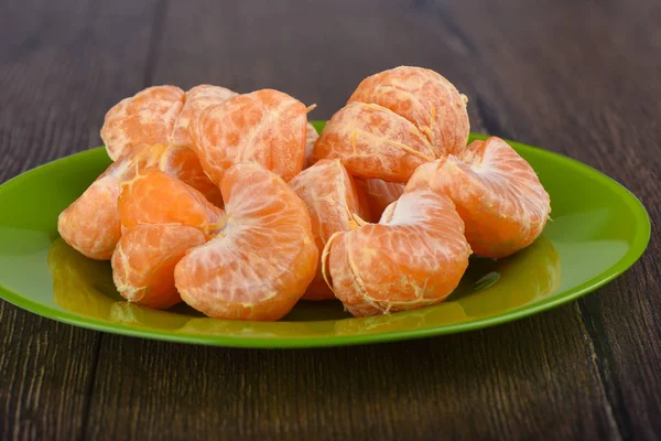 Trozos pelados de mandarinas en un plato verde sobre una mesa de madera — Foto de Stock