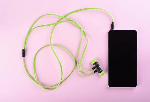 Green headphones connected to a smartphone isolated on a pink background. Accessories for individual listening to audio files.