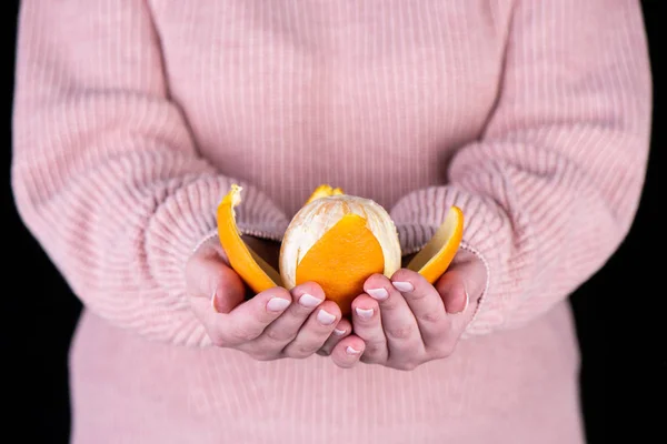 ピンクのセーターを持った少女の手のひらにオレンジをむいた. — ストック写真