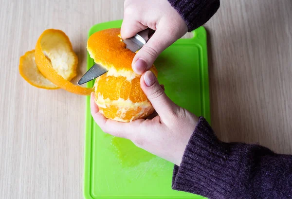 Mädchen putzt die Orange mit einem Messer. gesunde Ernährung. — Stockfoto