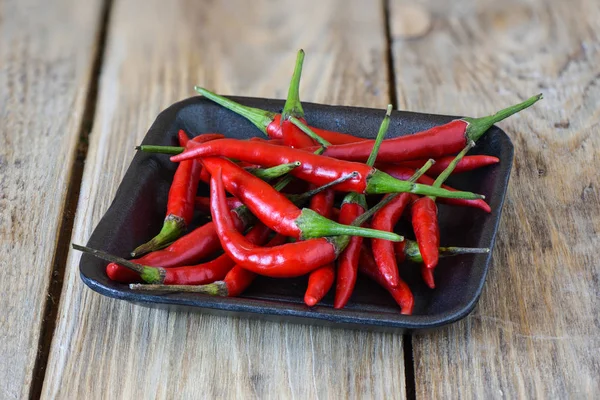 Pods of red hot pepper in a plastic tray on a wooden background. — Stock Photo, Image