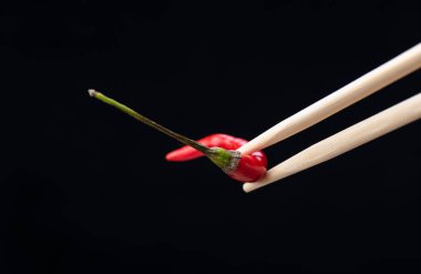 Siyah arka plan üzerinde izole kırmızı acı biber pod ile Chopsticks.