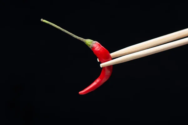 Chopsticks with red hot pepper pod isolated on black background. — Stock Photo, Image
