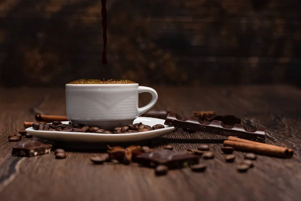 Menuangkan kopi hitam panas dari cezve ke dalam cangkir. Kopi kacang, coklat, bintang adas pada latar belakang kayu . — Stok Foto