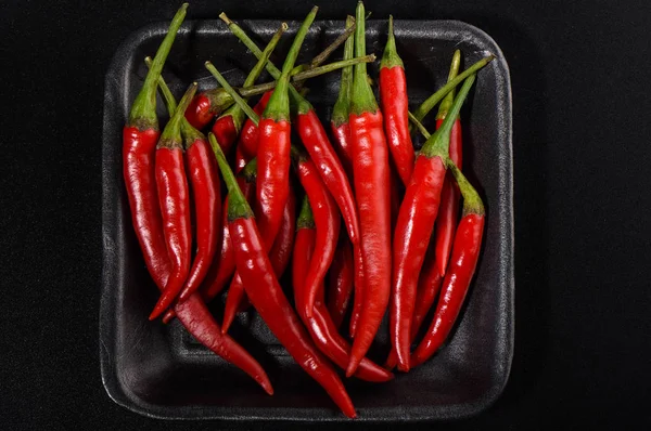 Pods of red hot pepper in a plastic tray on a black background. — Stock Photo, Image