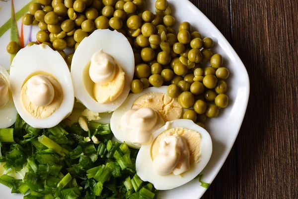 Gekookte eieren onder mayonaise met groene erwten en groene uien. Een traditioneel Russisch gerecht. — Stockfoto