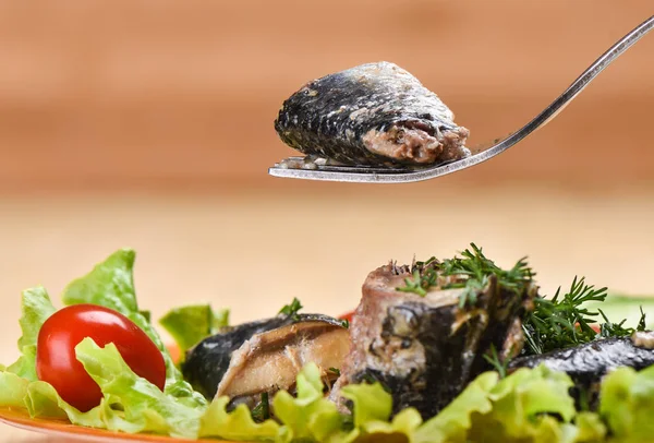 A piece of canned sardine Ivasi on a fork above a plate of sardines