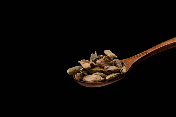 Семена кардамона на деревянной ложке на черном фоне . — стоковое фото