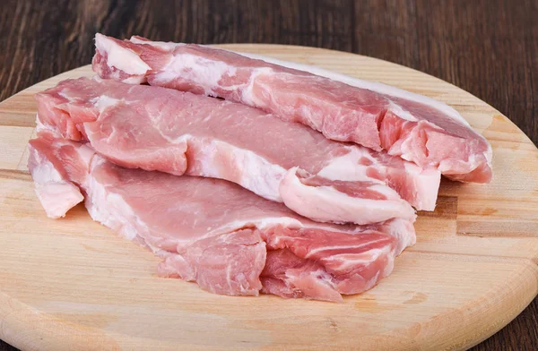 Bifes de porco em uma tábua de corte de madeira. Carne crua de porco para bifes . — Fotografia de Stock