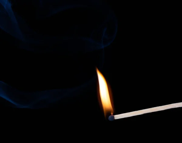 Burning wooden match with smoke over black background.