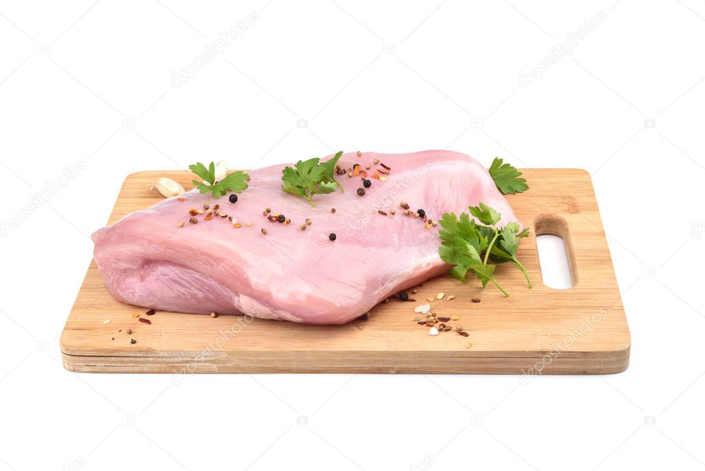 Raw turkey fillet with parsley and spices on a wooden cutting board over white background.