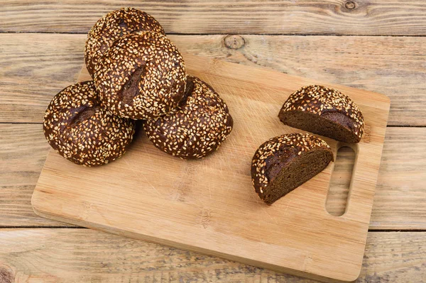 Солодовый хлеб с кунжутом на разделочной доске и деревянным столом. Нарезанный хлеб . — стоковое фото