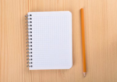 Ahşap masa üstü görünümünde kare kağıt defter. Not defterinin yanındaki kalem.