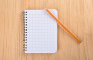 Ahşap masa üstü görünümünde kare kağıt defter. Bir defterin üzerine kalem.