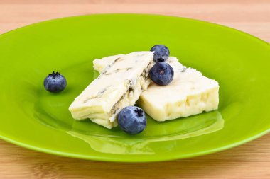 Yeşil bir tabakta lezzetli mavi kalıp peynir dilimleri üzerinde yaban mersini.