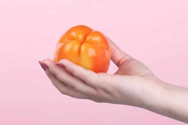 Orange süße Paprika in der Hand auf rosa Hintergrund. — Stockfoto