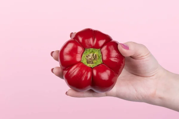 Röd söt paprika i handen över en rosa bakgrund — Stockfoto