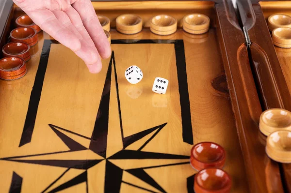 A hand throws white dice on a backgammon board.