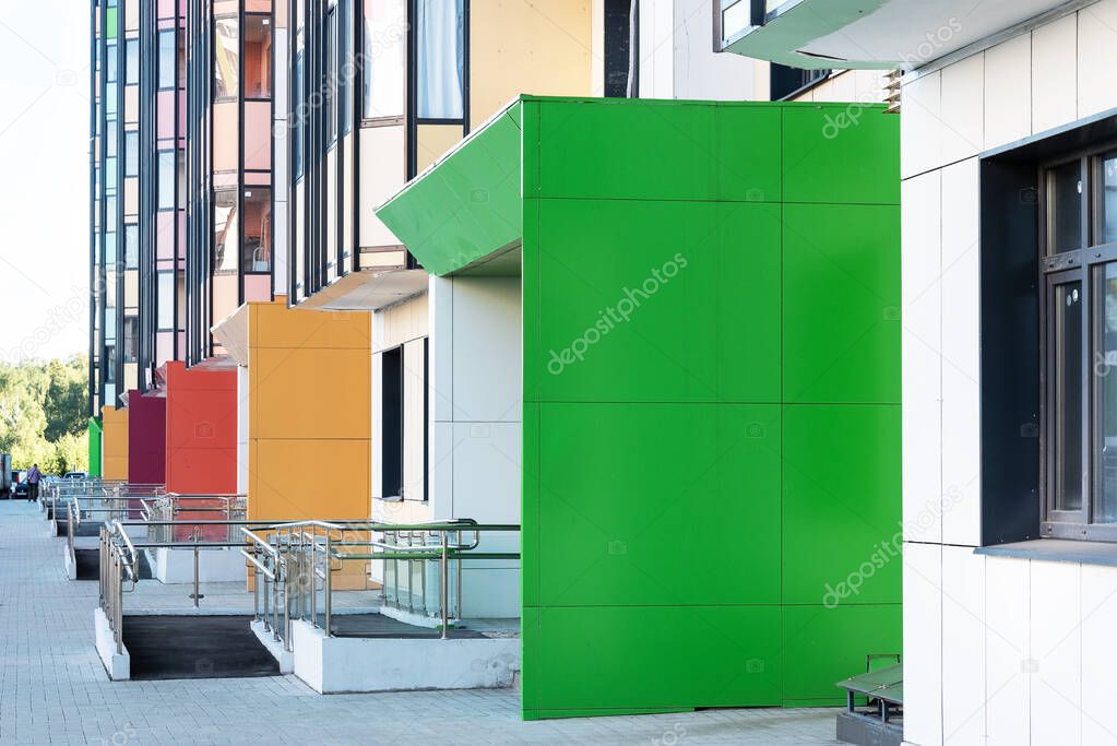 Part of the multi-colored facade of a multi-storey residential building with ramps at the entrance.