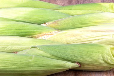 Tahta bir masada soyulmamış bir sıra çiğ mısır. Kırsal biçim.