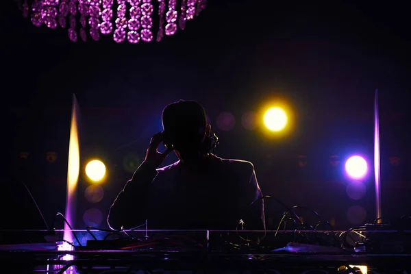 A disc jockey at the turntable. DJ mixing tracks on a mixer in a nightclub.DJ silhouette over foggy illuminated background.