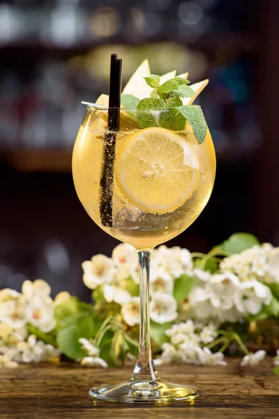 Летний коктейль, украшенный мятой, лимоном и ломтиками груш на деревянном столе на цветочном фоне — стоковое фото