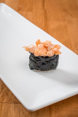 Sıcak bir arka plan üzerinde beyaz bir tabakta karidesli gunkan. Japon geleneksel suşi