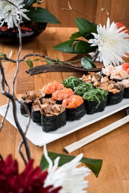 Çiçekler arasında beyaz tabakta somon balığı, yılanbalığı, chukka, karides ve tavuk etli ayarla Gunkan suşi. ahşap bacground. Geleneksel Japon mutfağı. yakın çekim