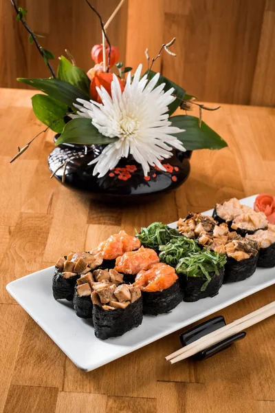 Çiçekler arasında beyaz tabakta somon balığı, yılanbalığı, chukka, karides ve tavuk etli ayarla Gunkan suşi. ahşap bacground. Geleneksel Japon mutfağı. yakın çekim