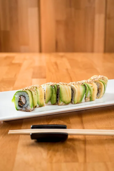 Dragon japonais à l'anguille et avocat avec gingembre, citron vert, sauce soja et baguettes sur une assiette blanche. isolé. gros plan — Photo