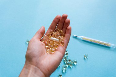 Uyuşturucuyla tedavi. Mavi arka planda el kapsülleri. Termometre. İlaçlar. Makro fotoğrafçılık, yumuşak odak.