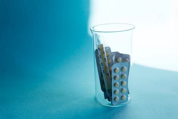 Treatment with drugs. Medicines, thermometer on a blue background in a flask. Macro photography, soft focus.