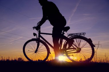 Adam bisikletin üstünde sürücü başlamak üzere. Arka plan günbatımı gökyüzü ve enerji alanıyla retro bisikleti rider silüeti